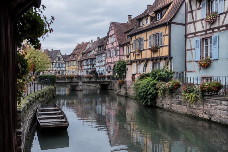 Pastel half-timbered houses along a Colmar canal in Little Venice, with a flat-bottomed boat moored.