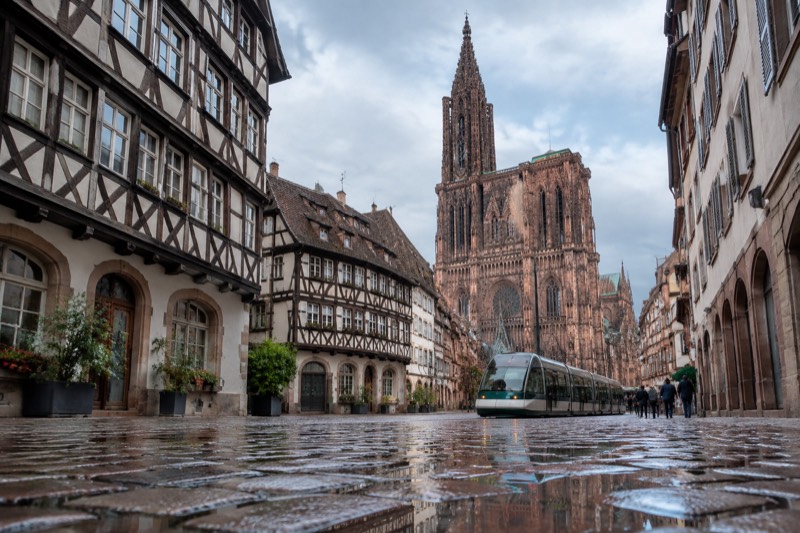 A cobbled street in the Grande Île with a tram passing and the cathedral spire above the rooftops