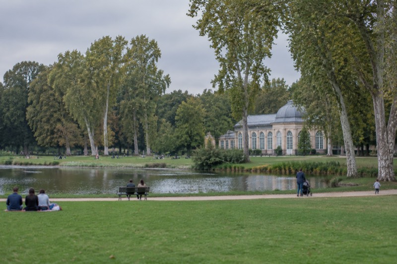 Wide lawns, a pond and tall plane trees in the Parc de l'Orangerie, families in the distance on a sunny day