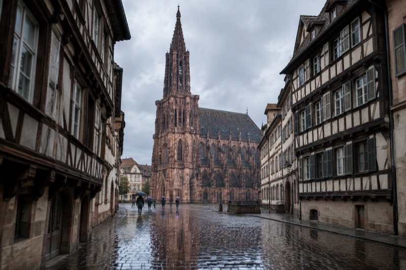 Wet cobblestones in the Grande Île reflecting the cathedral spire on a grey rainy day, a few umbrellas far away