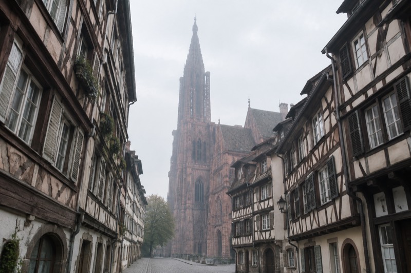 A cobbled street of half-timbered houses leading toward a tall cathedral spire in morning light, with no crowds.