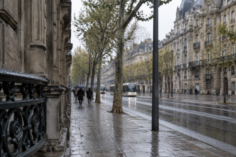 A wide avenue of grand grey sandstone buildings with a tram line running along it, in soft light.