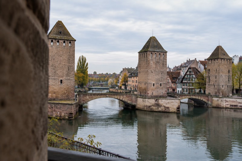 Three medieval stone towers on a canal with a dam behind them in soft afternoon light