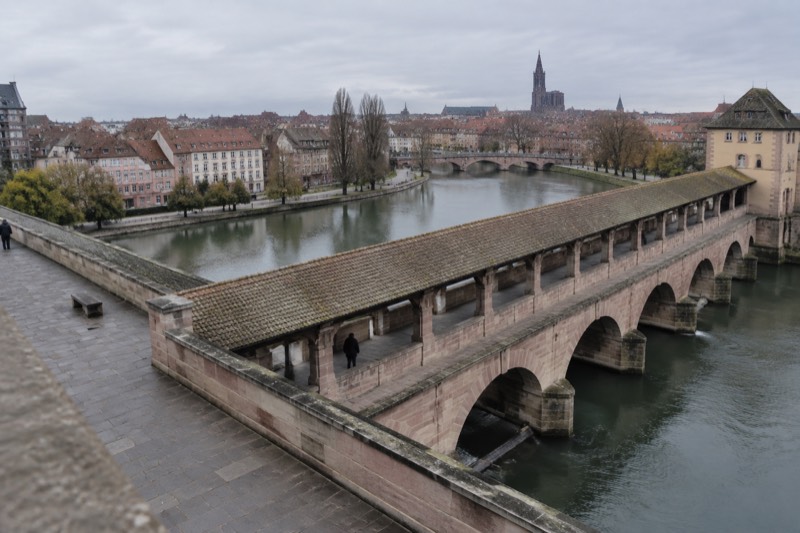 The covered arcade of the Barrage Vauban seen from its rooftop terrace, river and red roofs beyond.
