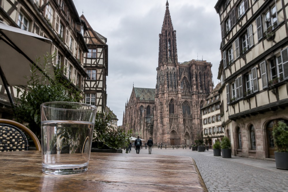A glass of water on a wooden table beside a half-timbered Strasbourg street