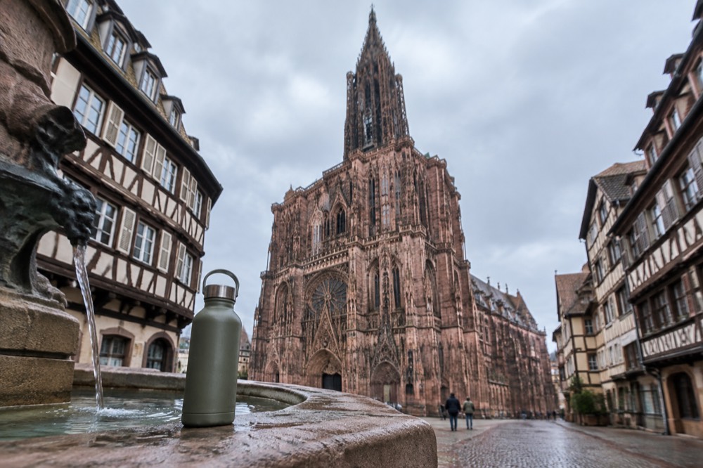 A refillable water bottle resting on a stone fountain edge in a Strasbourg square