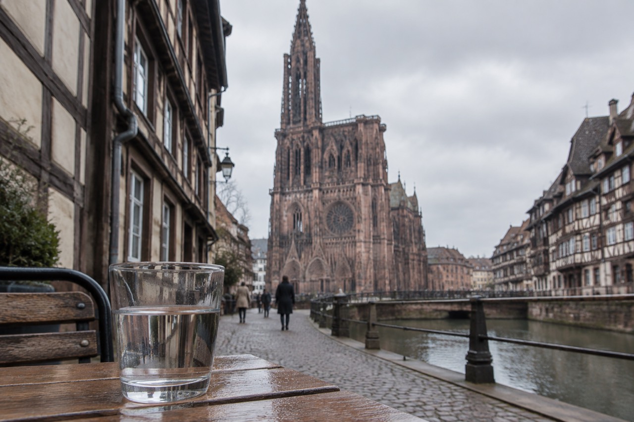 A glass of water on a wooden table beside a half-timbered Strasbourg street