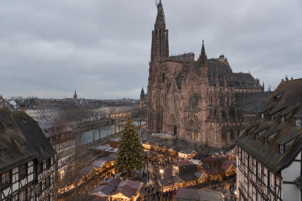 Christmas market chalets and a decorated tree in a floodlit square in Strasbourg at dusk