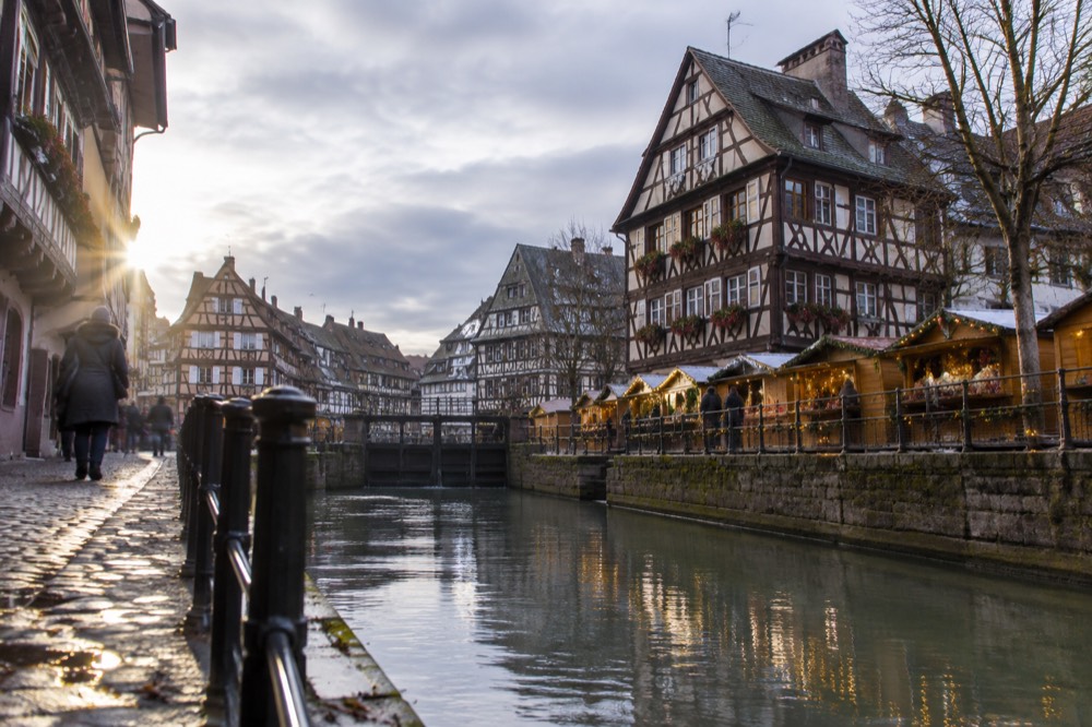 Illuminated Christmas chalets along a canal in Petite France with half-timbered houses behind