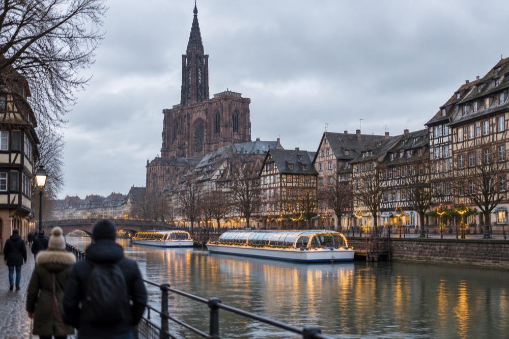Festively lit river boats moored on the Ill in Strasbourg at dusk with half-timbered houses behind
