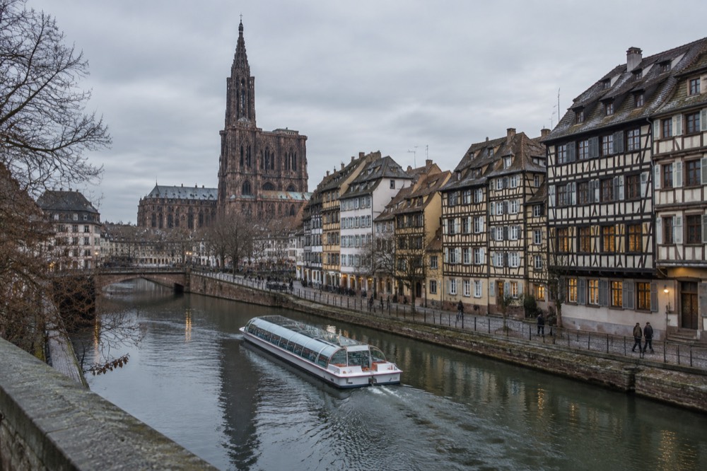 A sightseeing boat passing illuminated half-timbered buildings along the Ill in Strasbourg in December