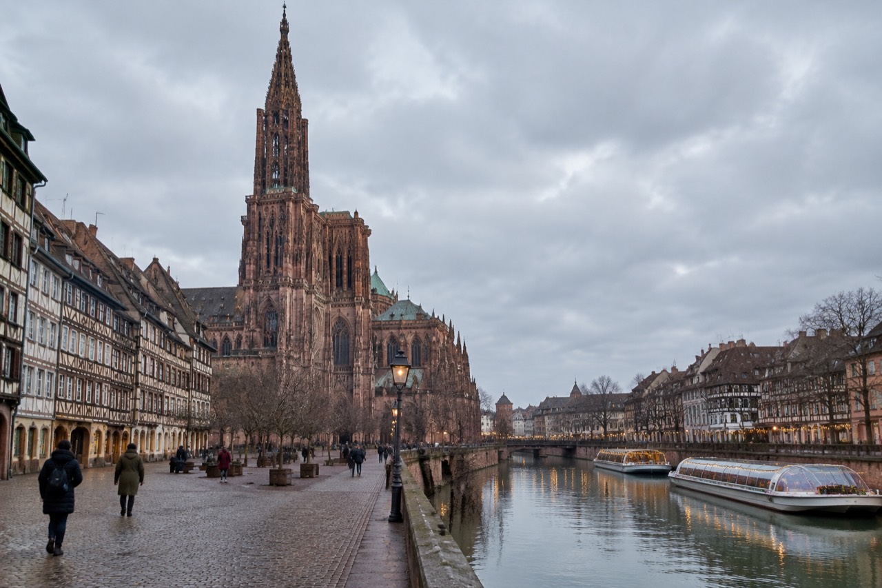 Festively lit river boats moored on the Ill in Strasbourg at dusk with half-timbered houses behind