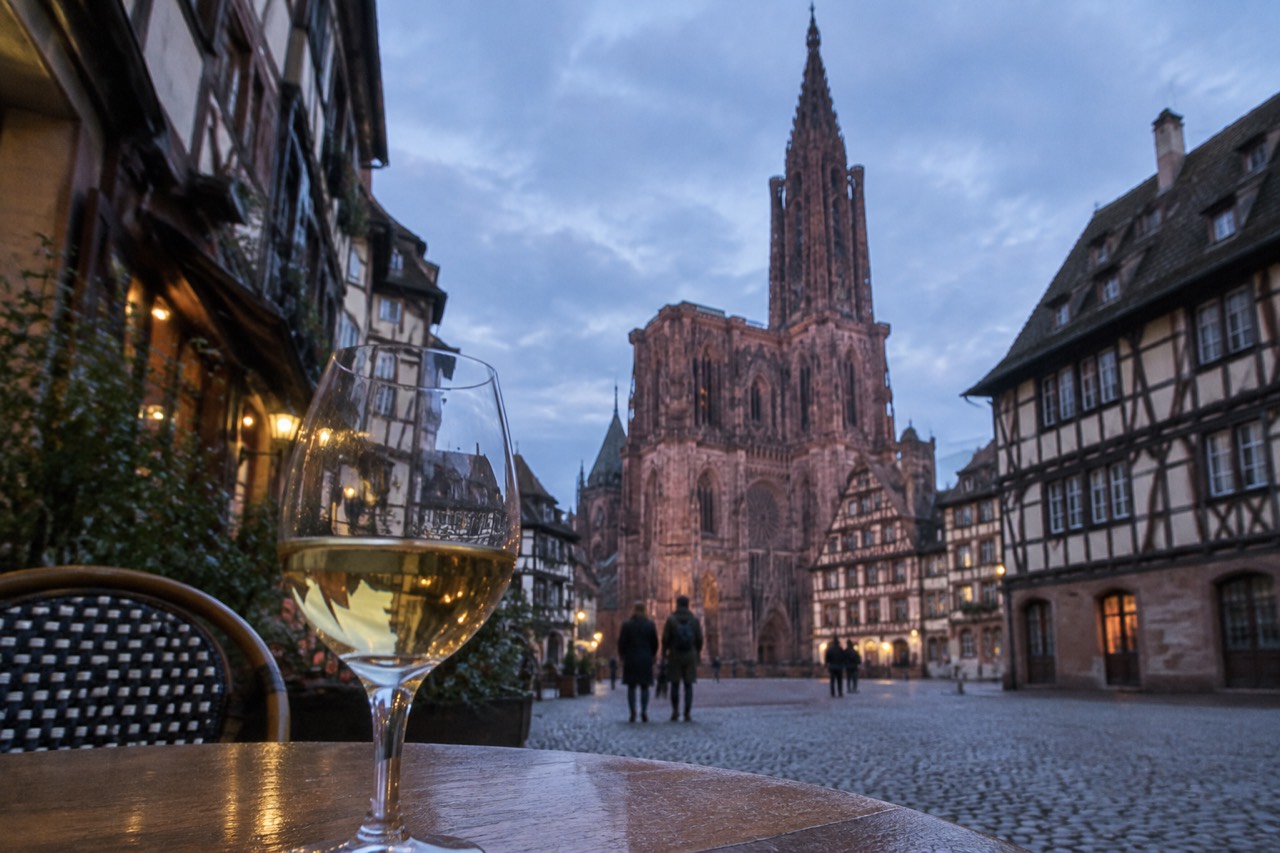 A glass of white wine on a wooden table beside half-timbered houses in Strasbourg