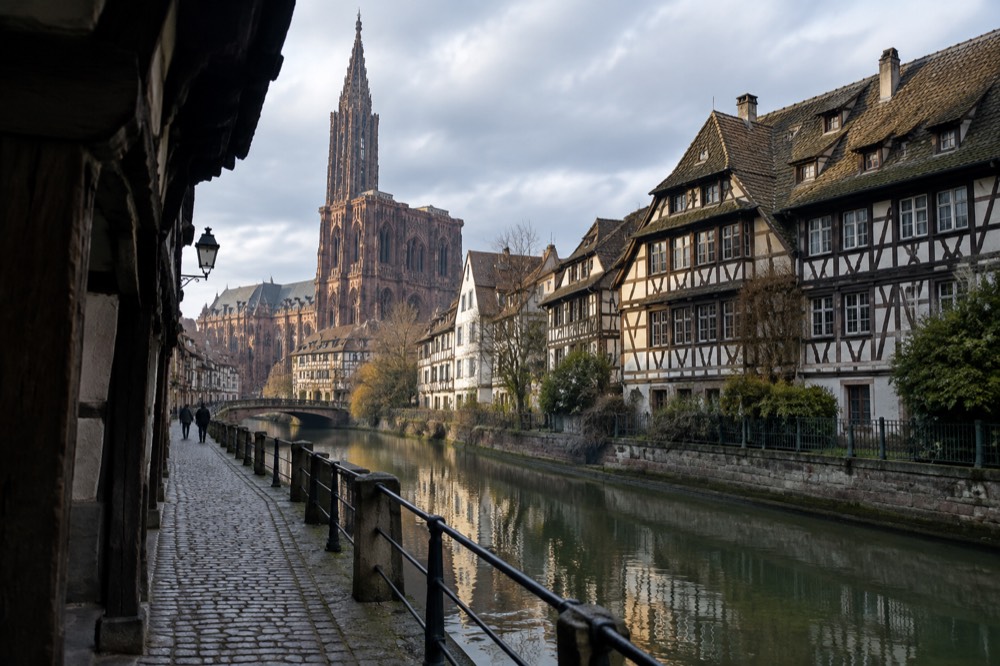 Half-timbered houses reflected in a quiet canal along a cobbled lane in central Strasbourg