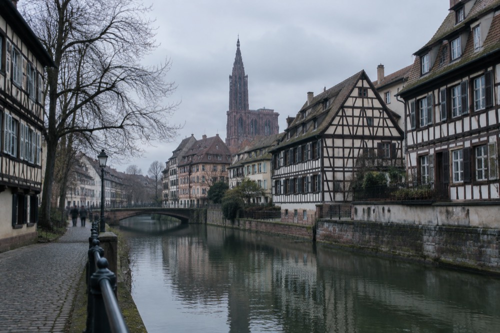 Half-timbered houses along a canal in Strasbourg with the cathedral spire rising beyond the rooftops