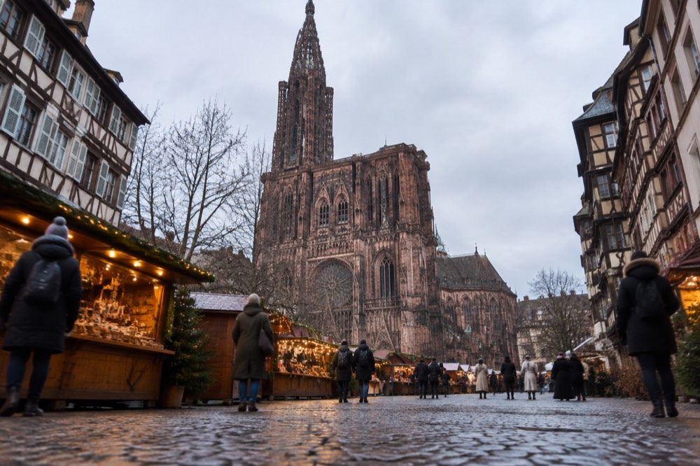 Wooden market chalets with warm lights standing in a square beside a tall gothic cathedral