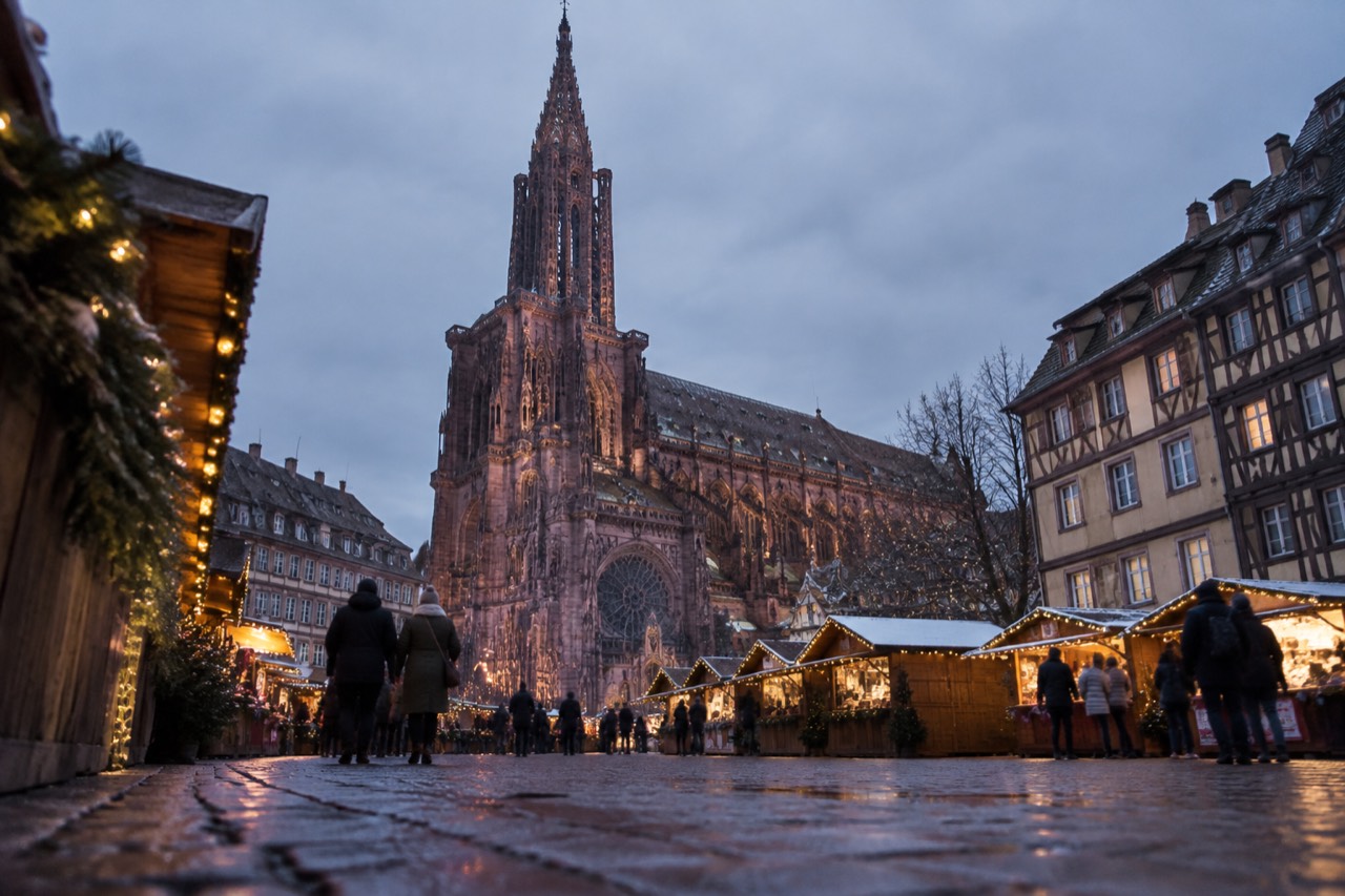 Festively lit wooden chalets in a square beside Strasbourg Cathedral at dusk