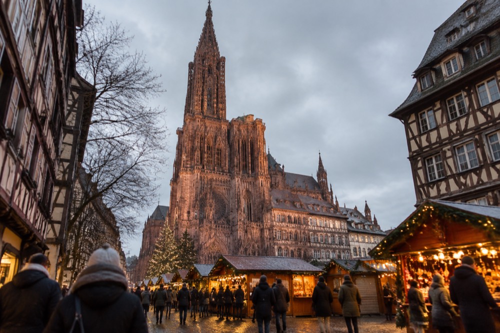 Festively lit market chalets in front of a cathedral at dusk