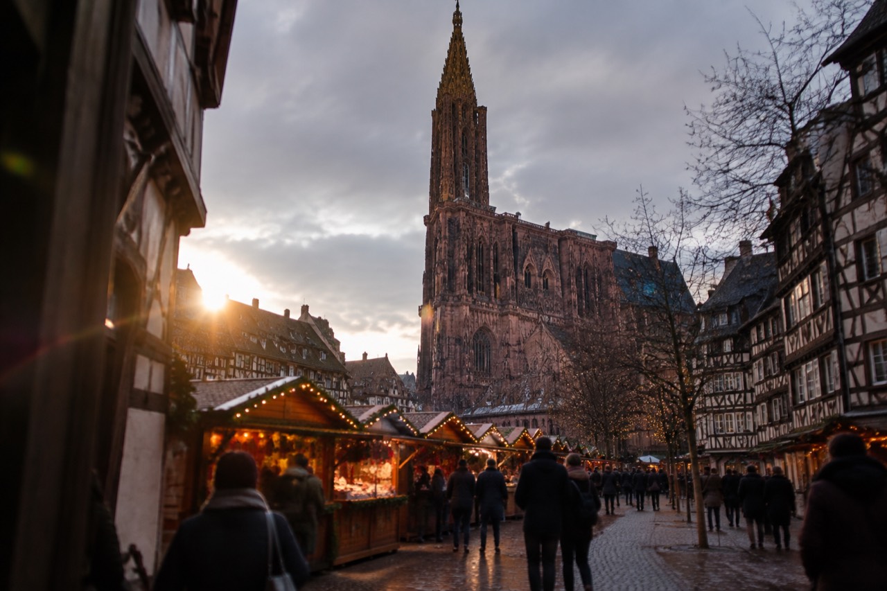 Festively lit market chalets in front of a cathedral at dusk