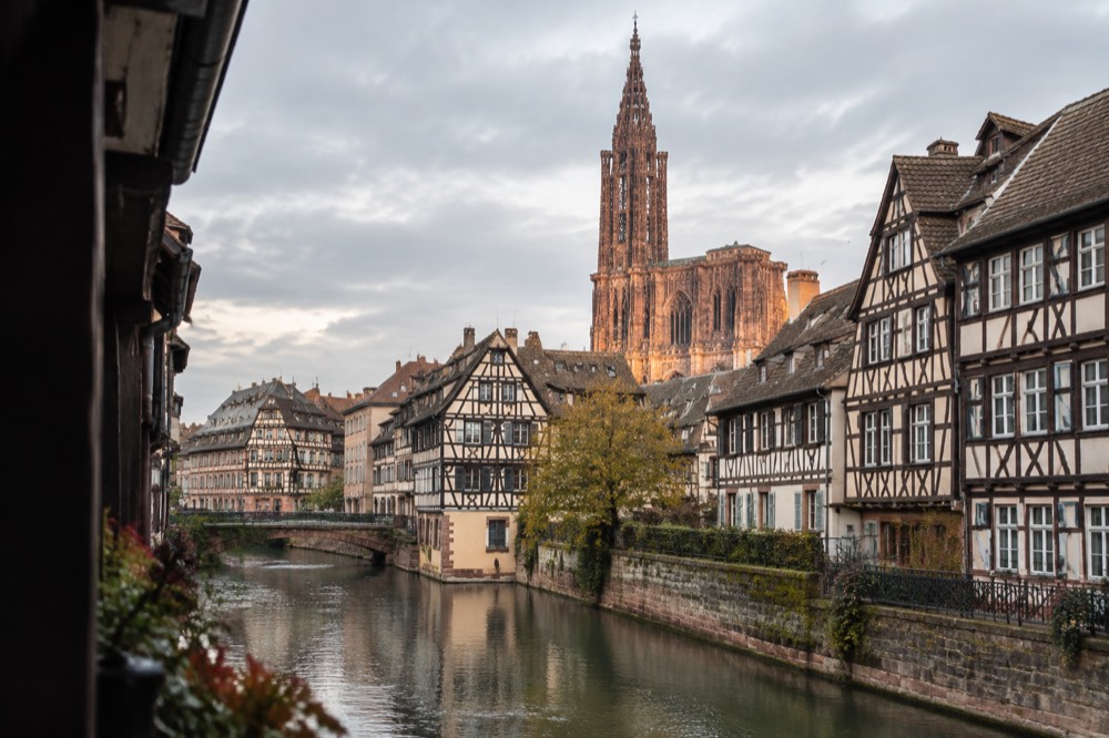 Half-timbered buildings along a canal in Strasbourg with the cathedral spire rising behind the rooftops