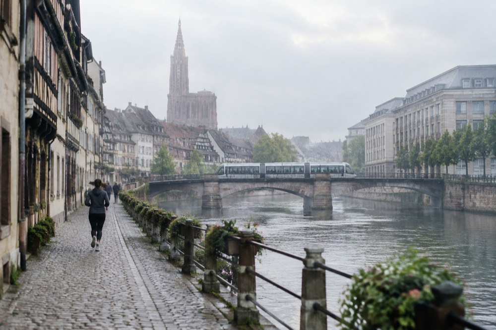 Trams crossing a bridge over the Ill with modern institutional buildings along the far bank
