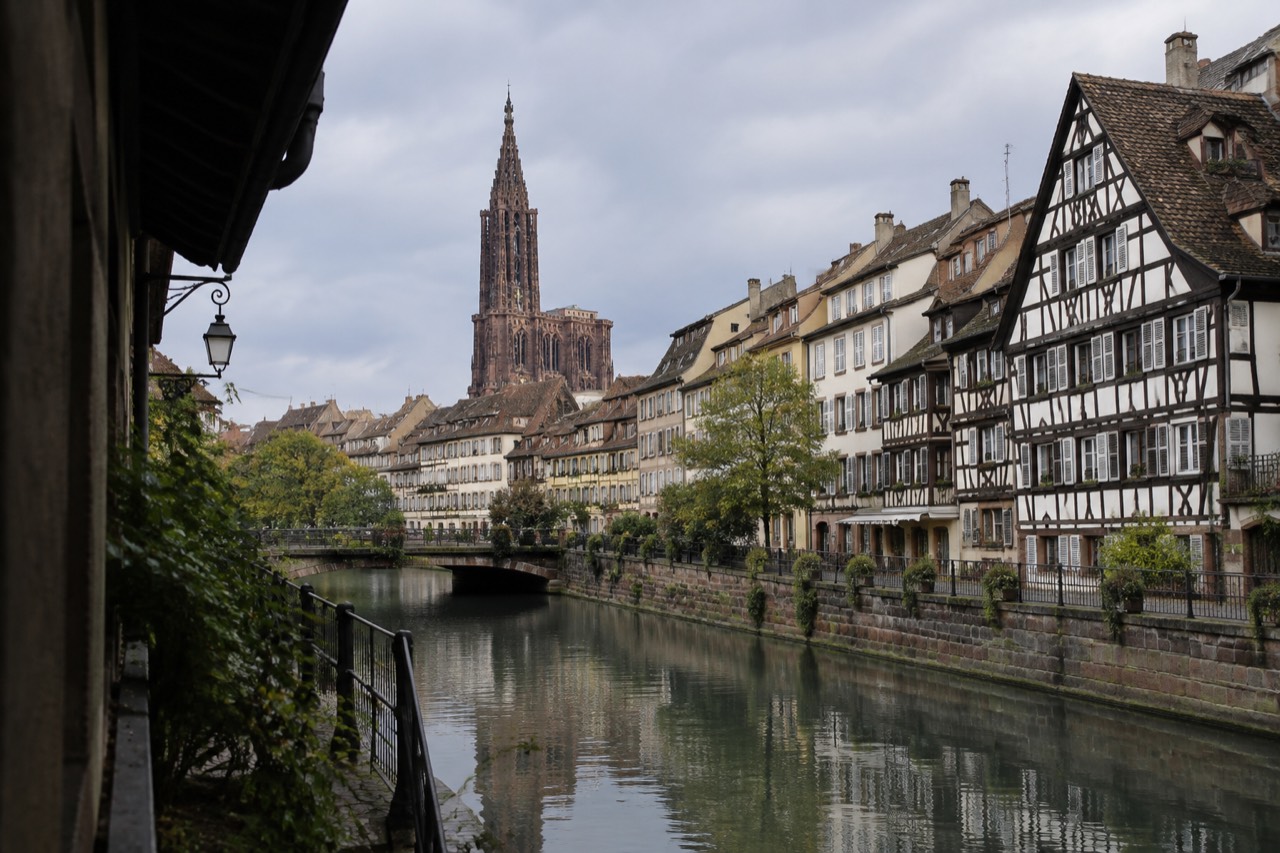 Half-timbered buildings along a canal in Strasbourg with the cathedral spire rising behind the rooftops