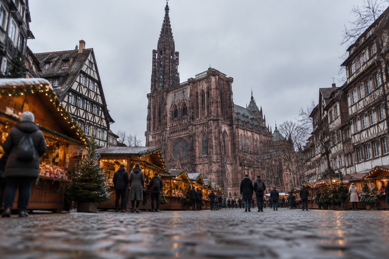 Festive wooden chalets with glowing garlands in front of Strasbourg Cathedral at dusk