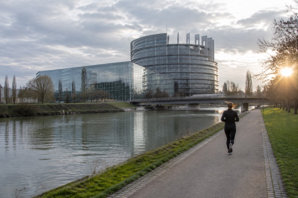 The modern glass facade of the European Parliament chamber building in Strasbourg rising above the River Ill