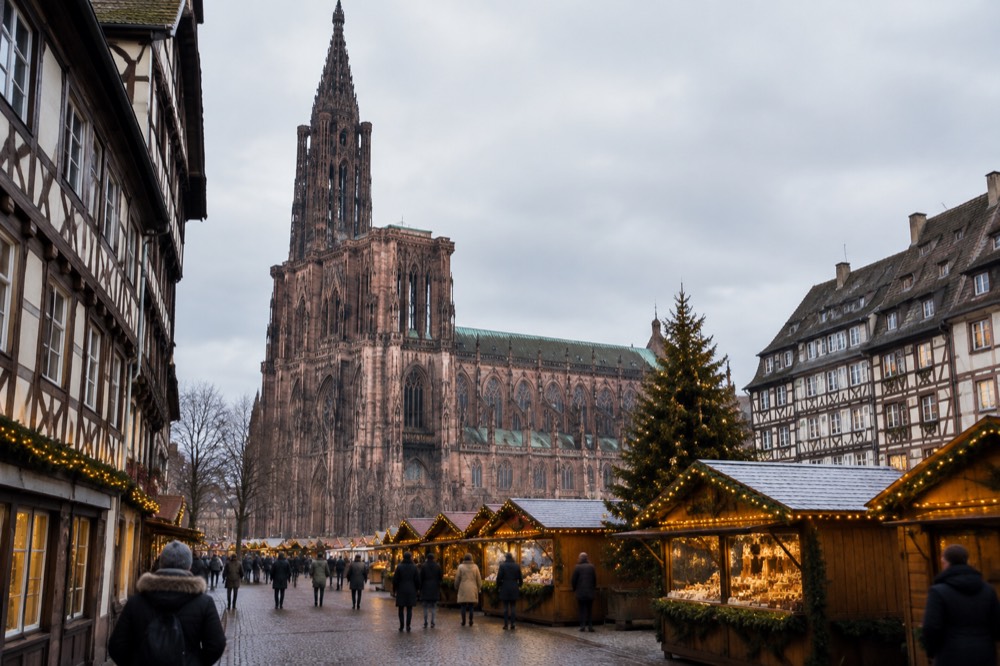 Festive chalets and illuminated half-timbered buildings around a Christmas market square in Alsace at dusk