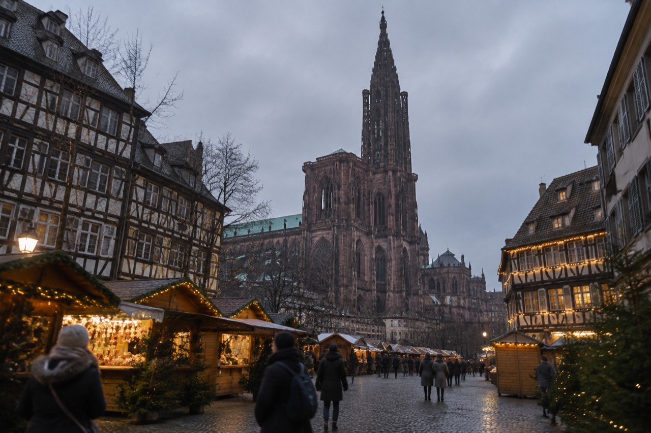 Festive chalets and illuminated half-timbered buildings around a Christmas market square in Alsace at dusk