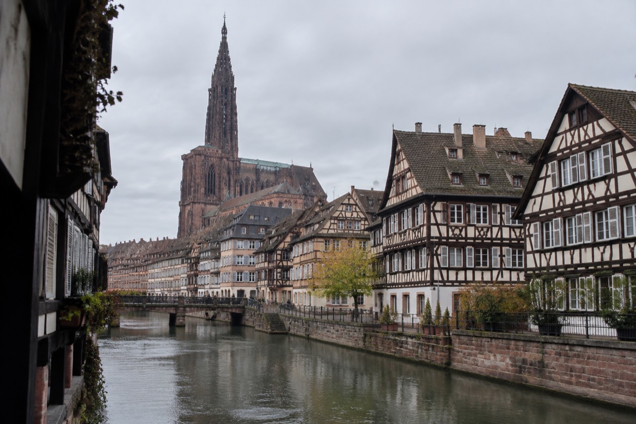 Half-timbered houses along a canal in Strasbourg with the cathedral spire rising behind the rooftops