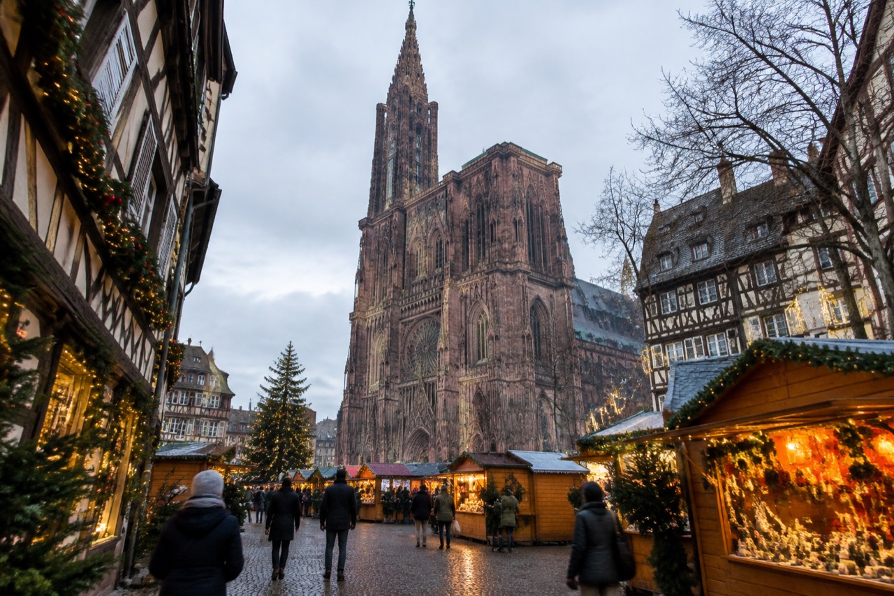 Illuminated Christmas market chalets and decorated facades around Strasbourg Cathedral at dusk