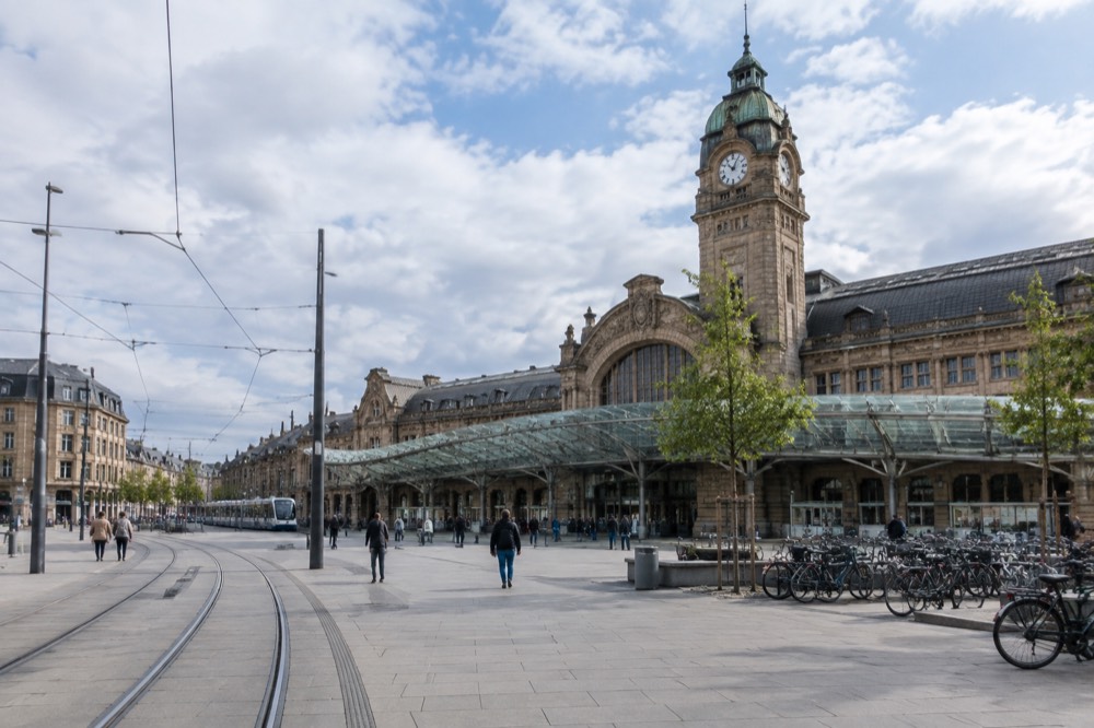 The grand stone facade of Strasbourg's main railway station with its historic clock tower rising above the forecourt