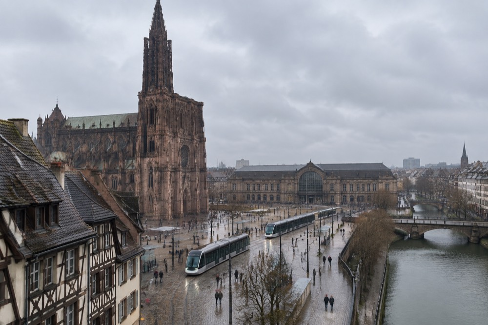 Trams crossing the open plaza in front of Strasbourg railway station with the station facade in the background