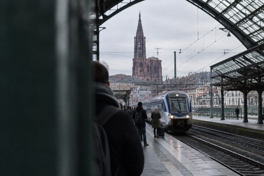 Travellers waiting on a platform at Strasbourg railway station as a train arrives under the glass roof