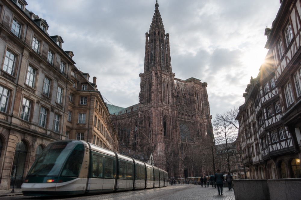 A tram passing stone buildings on the edge of the Strasbourg Old Town