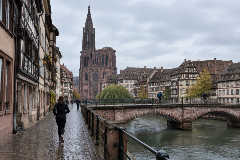 Cyclists crossing a Strasbourg bridge over the River Ill with half-timbered houses behind