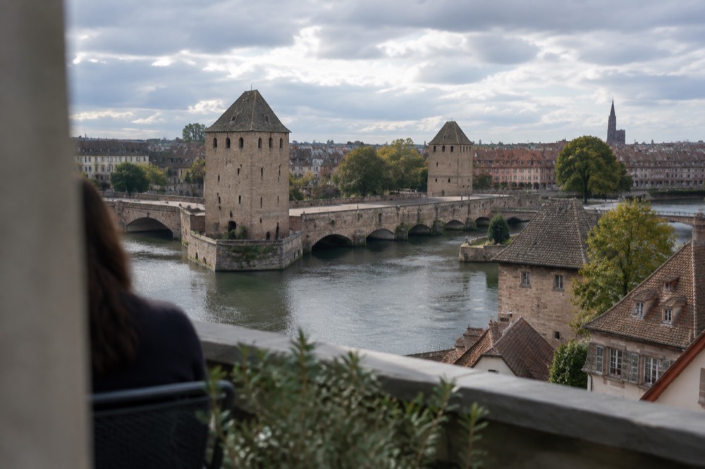 View from a rooftop terrace over river channels, stone towers and tiled roofs of an old quarter