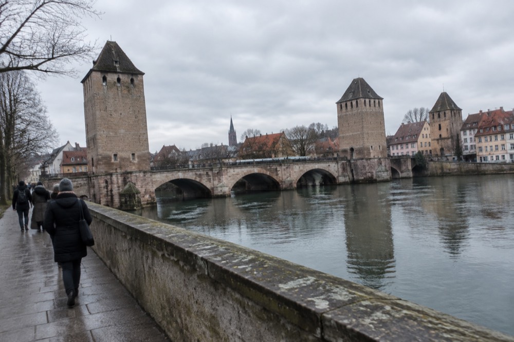 A stone terrace walkway above a river with winter light on old towers and rooftops