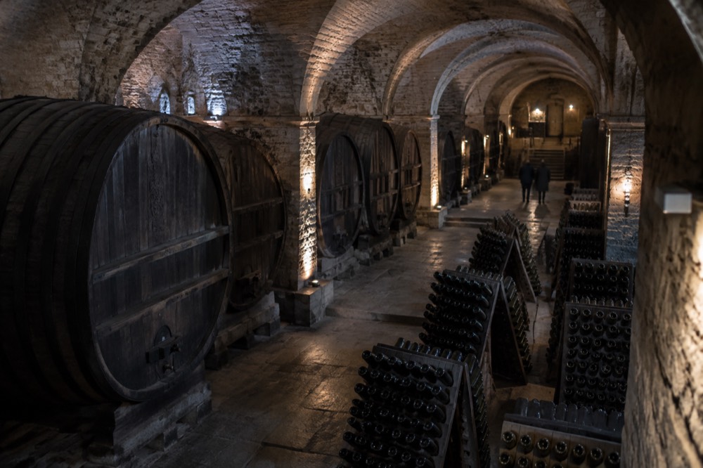Bottles of Alsace wine resting in racks inside a dim historic cellar
