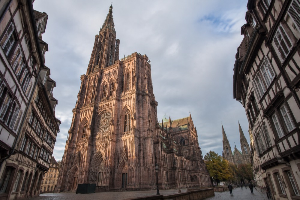 Gothic revival church with twin spires rising above trees along a quiet Strasbourg street