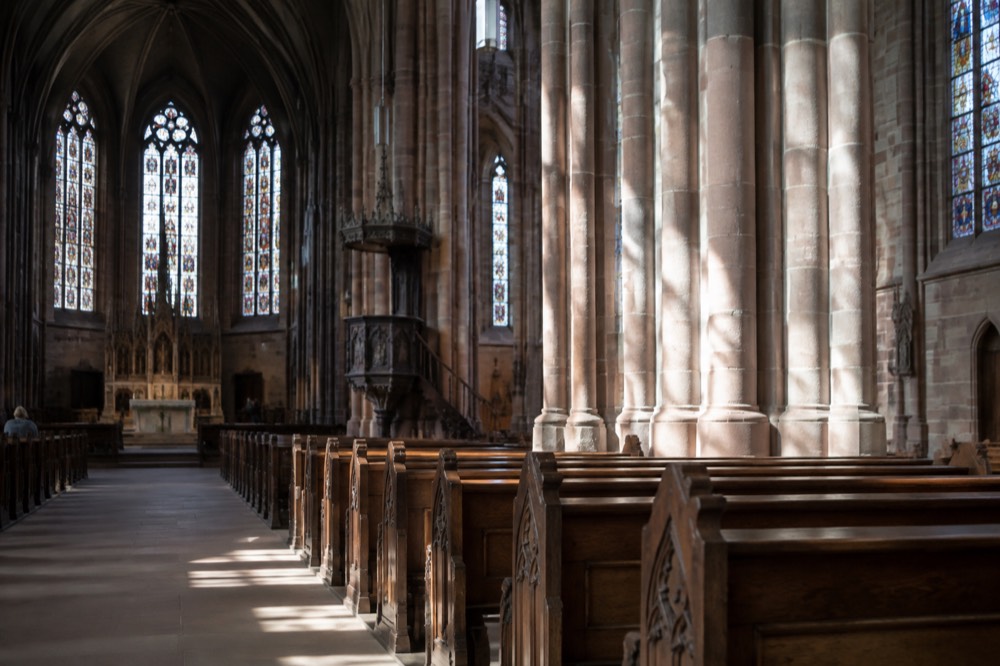 Sunlight falling on stone columns and wooden pews inside a large Alsatian church