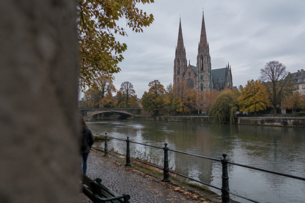Church spires seen across autumn trees and a calm stretch of the Ill river