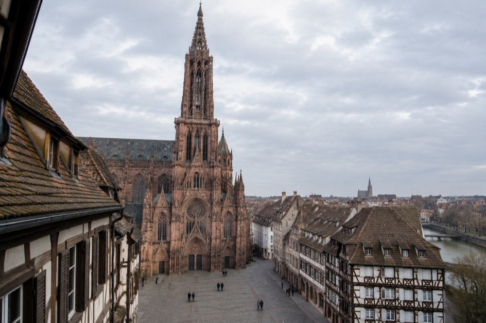 The pink sandstone facade and tall tower of a historic church on a quiet square in Strasbourg