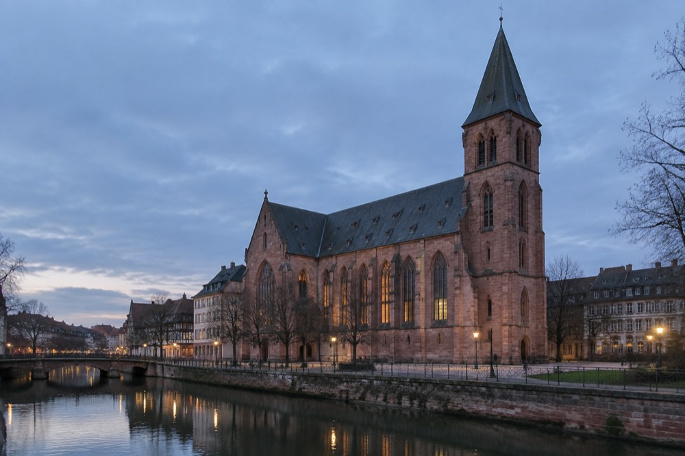 A vast church interior with tall stone columns, clear glass windows and an organ gallery at the far end