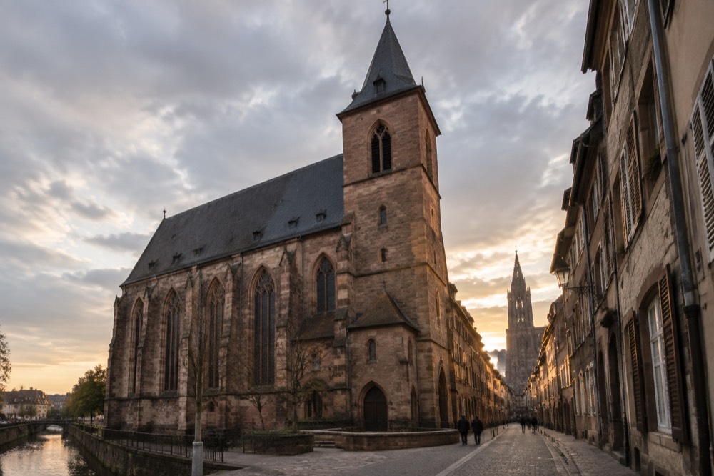 A narrow old street of tall stone houses leading towards a cathedral tower in Strasbourg