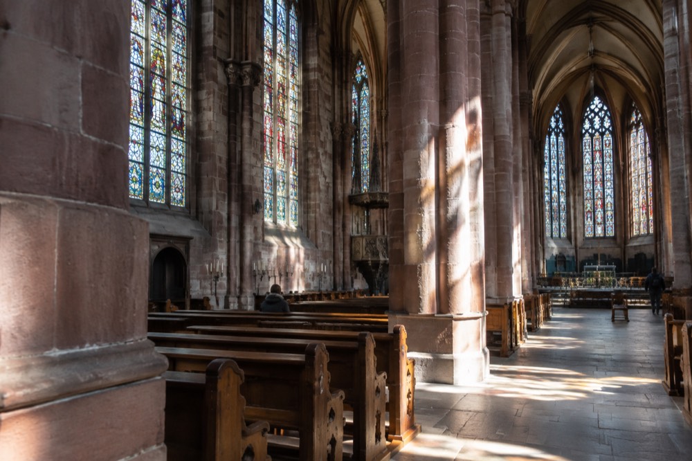 Sunlight falling through clear glass windows onto stone columns inside a large hall church
