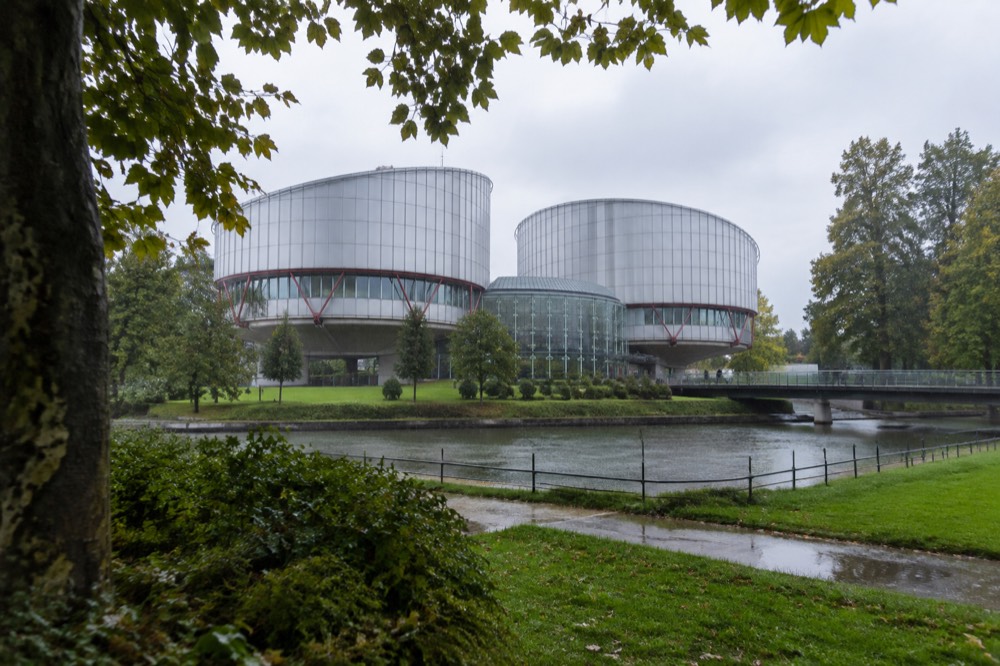 A curved modern courtroom drum seen from a landscaped lawn with mature trees