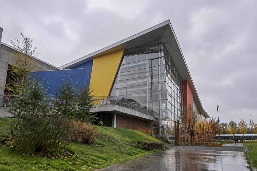 The modern glass and steel facade of a science centre building beside a landscaped park