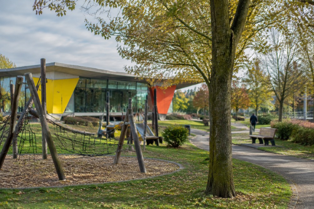 A landscaped park path with mature trees beside a modern public building